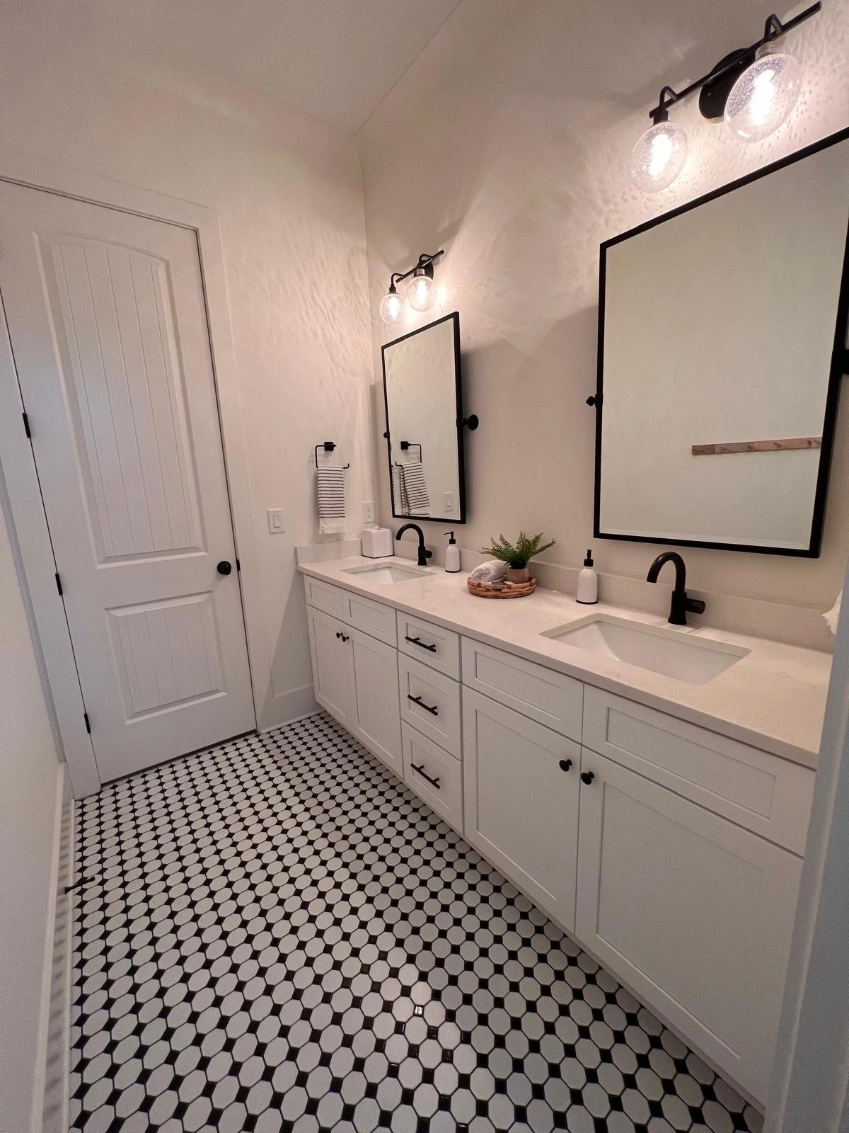 Double vanity with black-framed mirrors and mosaic tile flooring