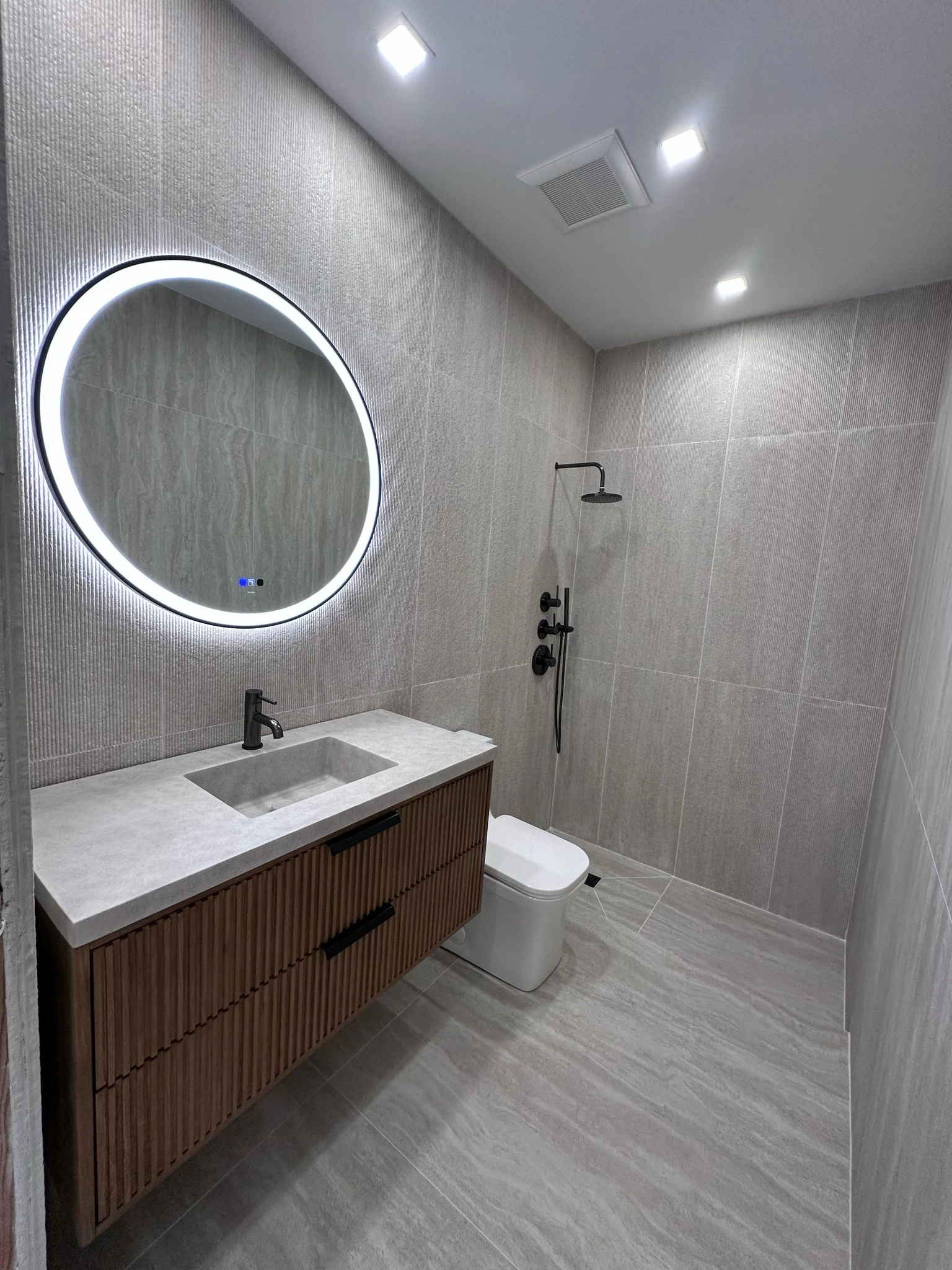 Grey tile bathroom with round backlit mirror and floating wood vanity — Davie, FL
