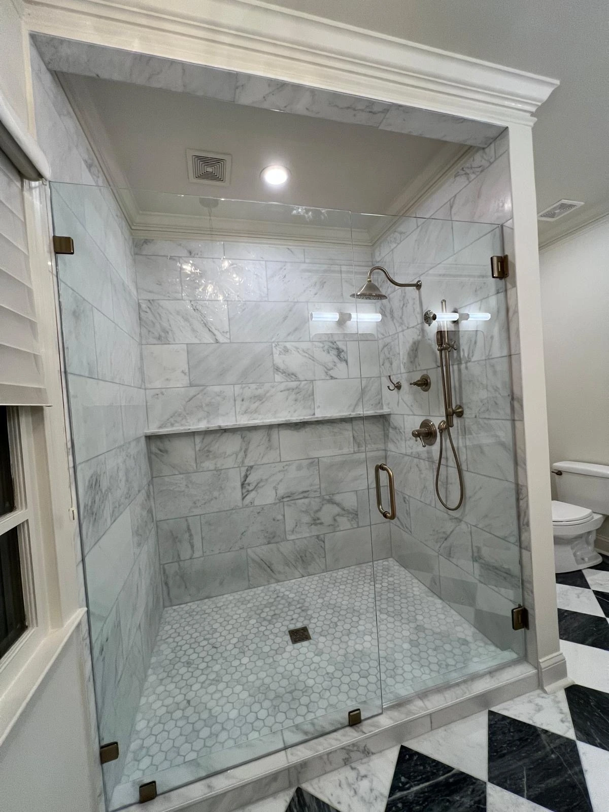 Walk-in shower with marble tile surround and black-and-white checkered floor in a South Florida bathroom remodel