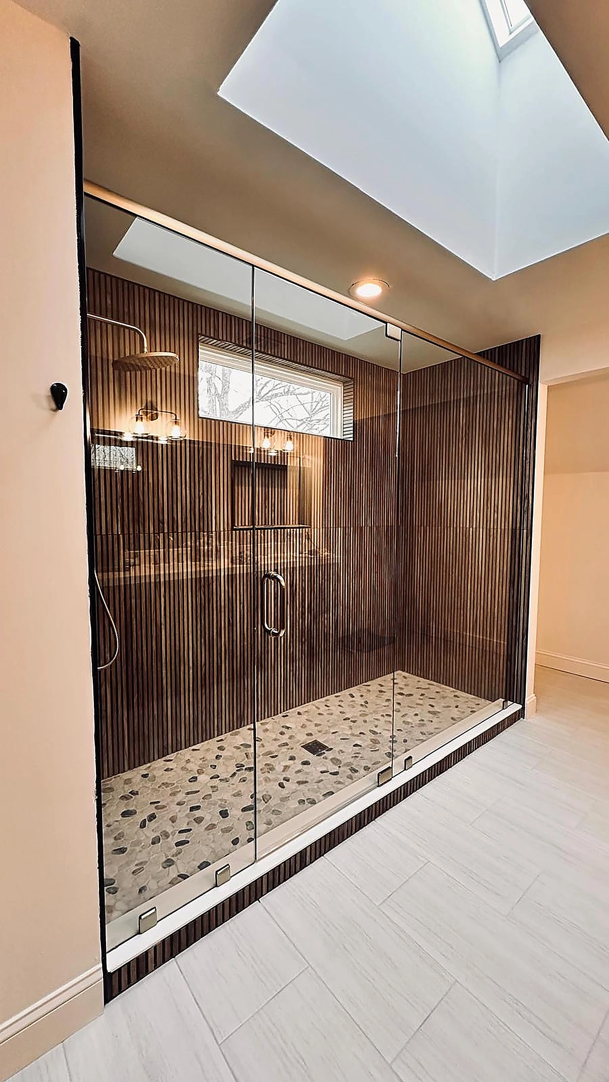 Wood-look ribbed tile shower with framed glass door and pebble floor