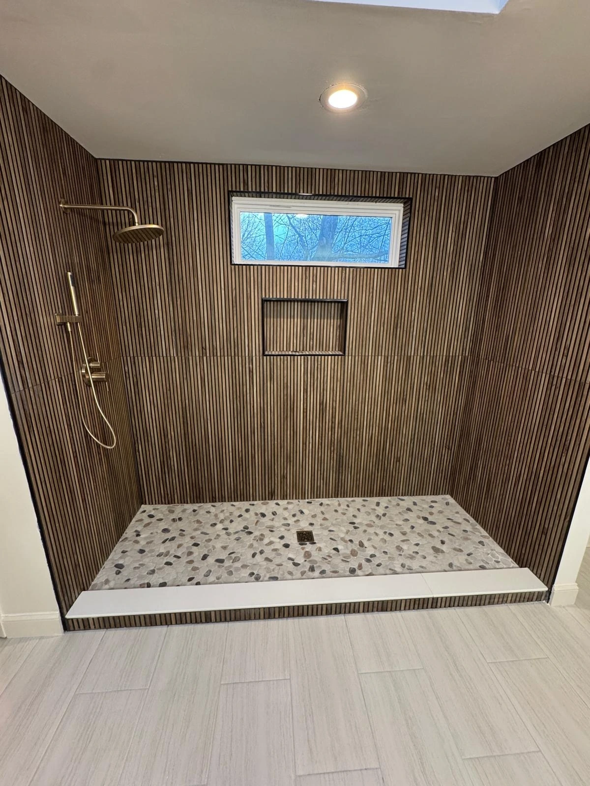Wide ribbed wood-look tile shower with pebble stone floor