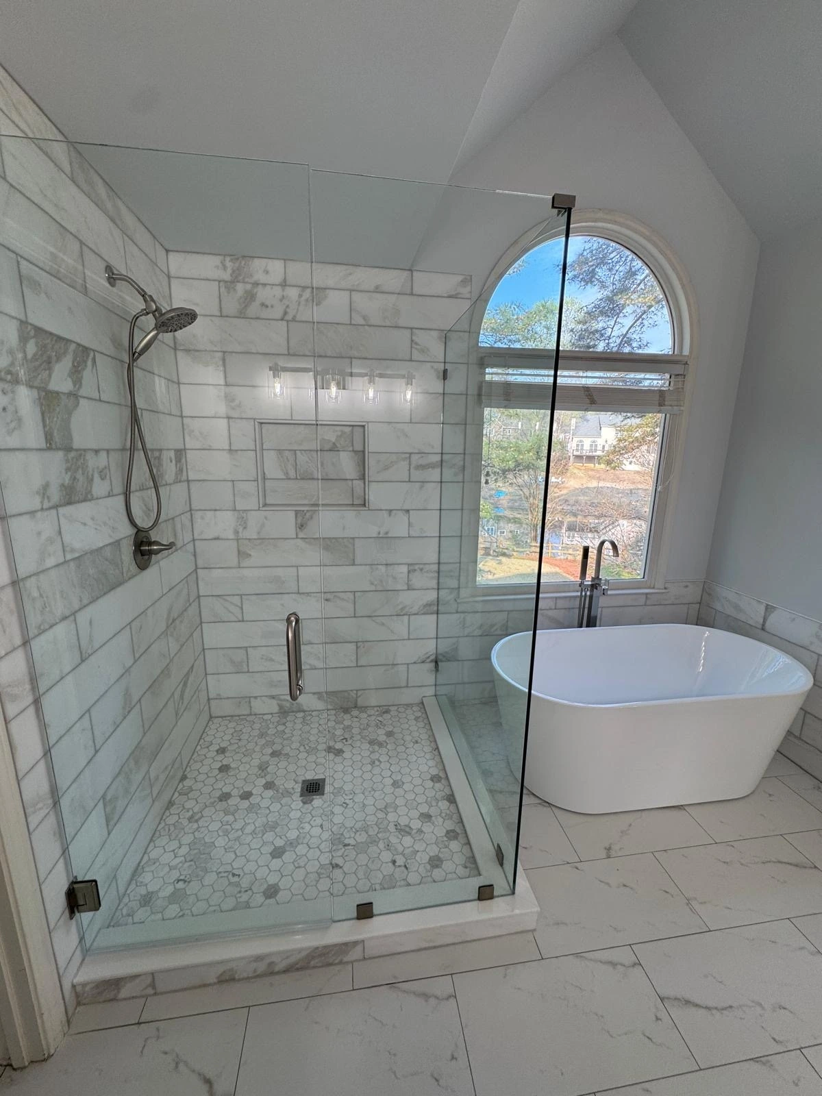 Glass shower and freestanding tub under an arched window