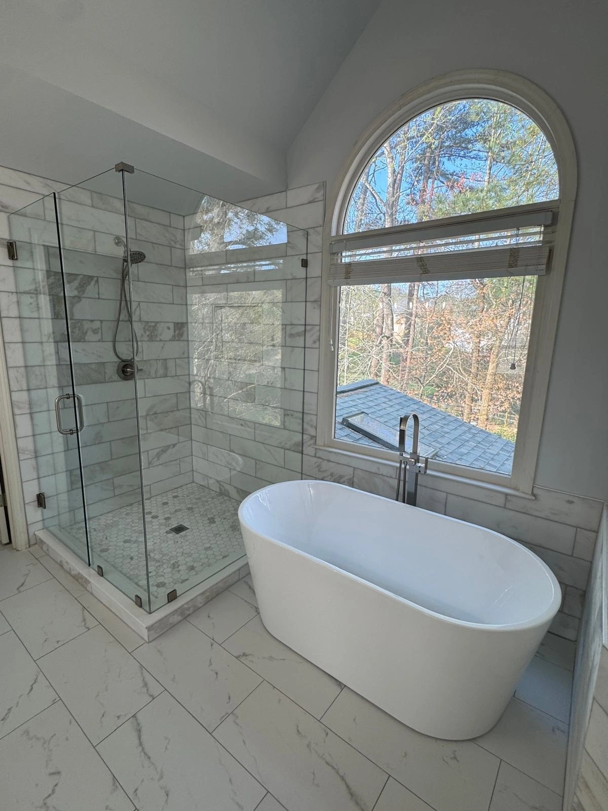 Freestanding tub and glass shower beneath an arched window