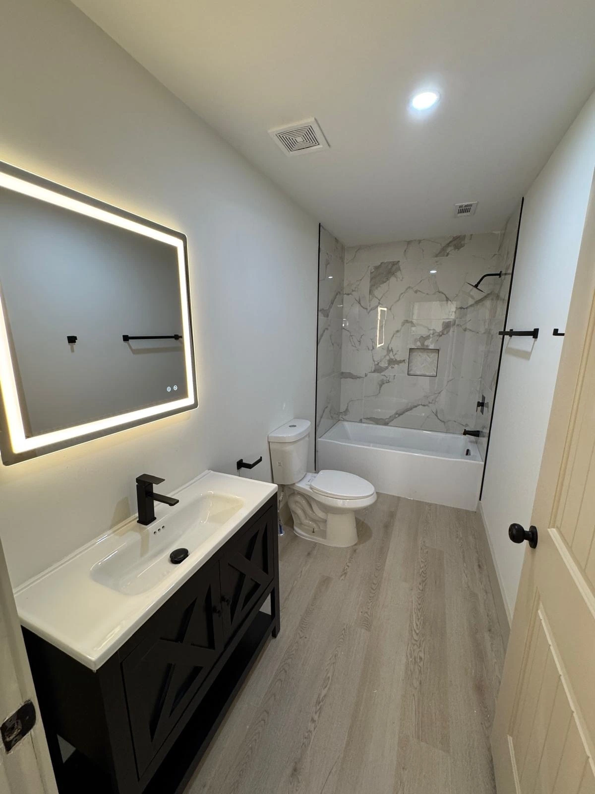 Compact bathroom remodel with marble tub-shower surround and black vanity — Boynton Beach, FL
