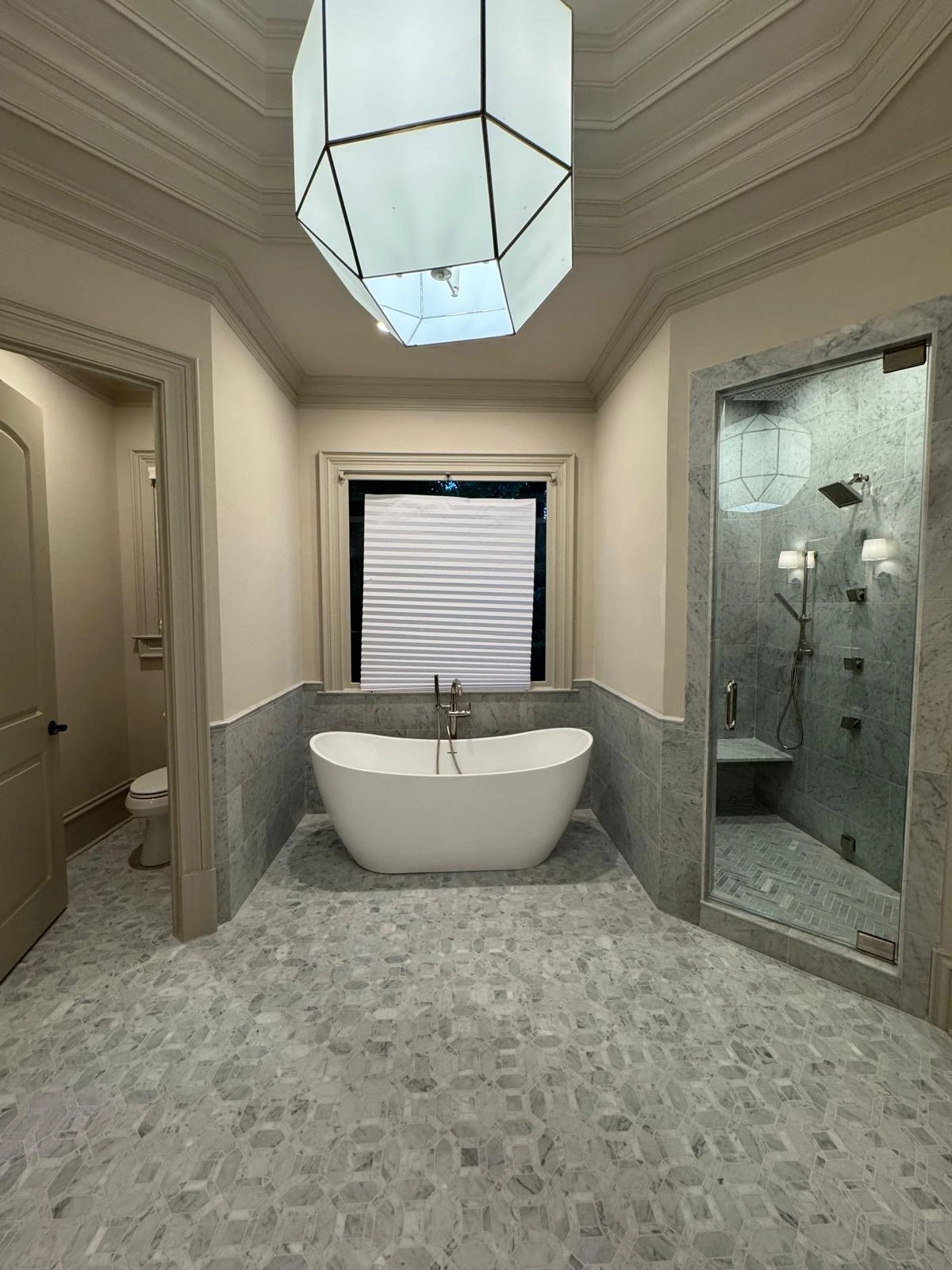 Soaking tub and shower with pebble flooring under a pendant light