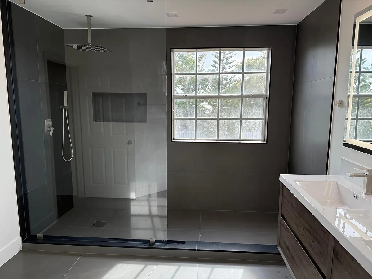 Dark tile walk-in shower with window and wood vanity