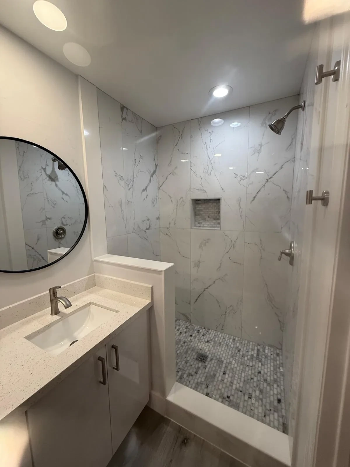 Bathroom remodel with marble shower surround, quartz vanity and round mirror